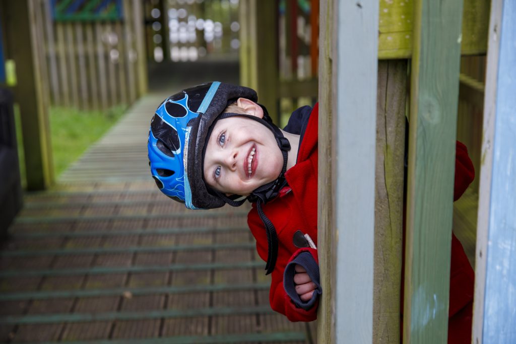 Young boy peeping out from a fence, wearinfg a bike helmet