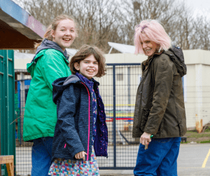 Playworker, a parent and a young person outside looking back abd smiling at the camera