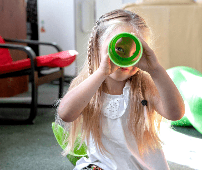 Young blonde girl smiling through a green tube