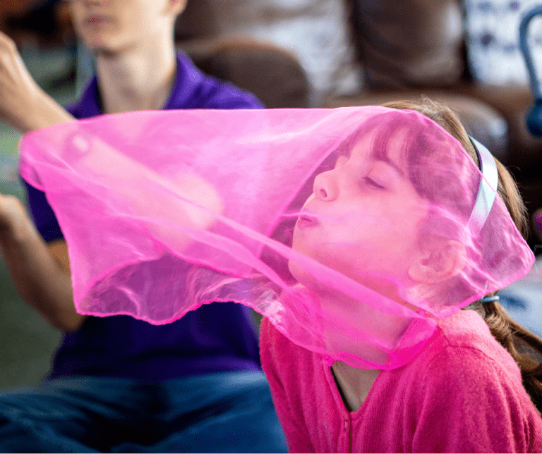 Young female blowing a pink piece of fabric that's draped over her face.