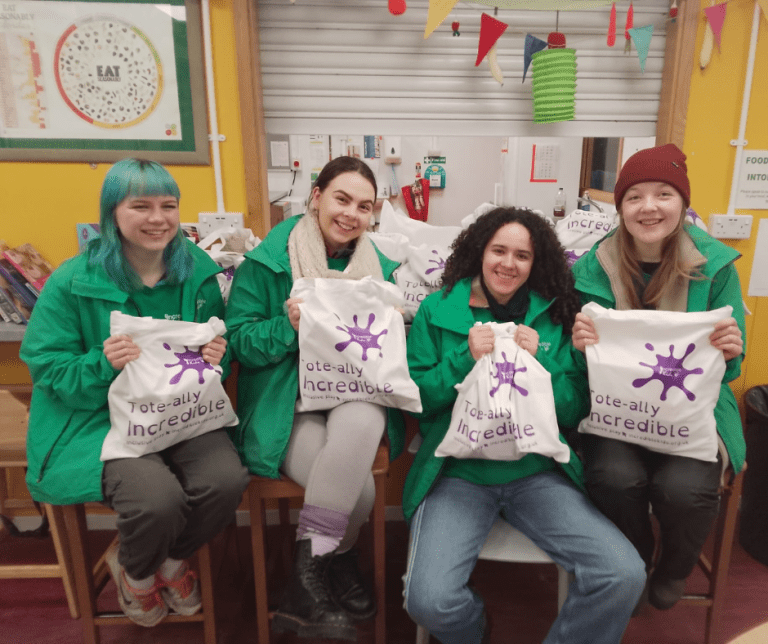 Group of young women in Incredible Kids green hoodies smiling at the camera with tote goody bags