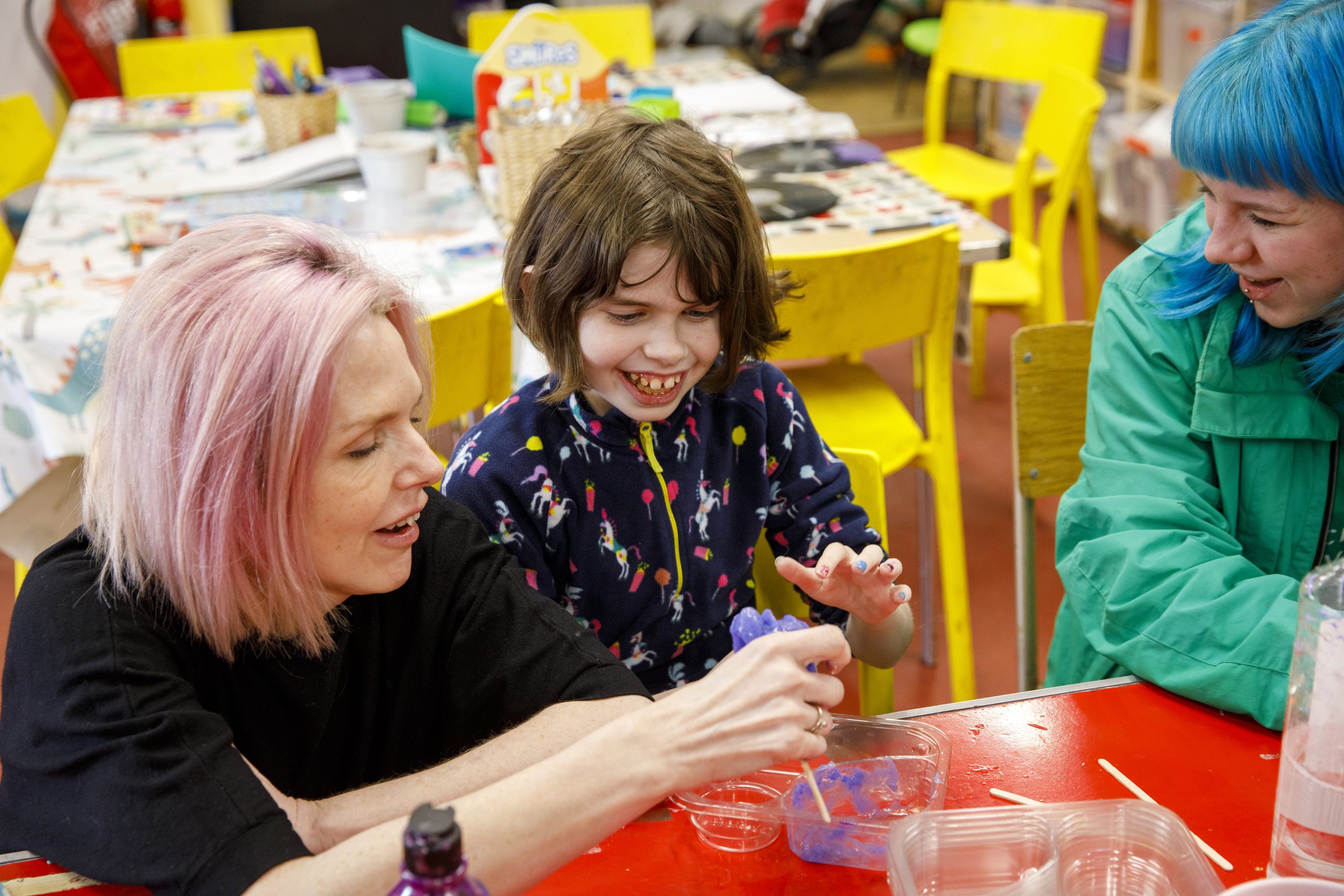Young person smiling next to an adult playing with slime