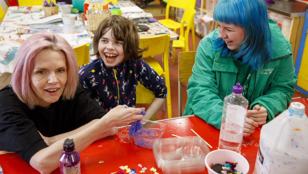 Young person smiling next to an adult playing with slime